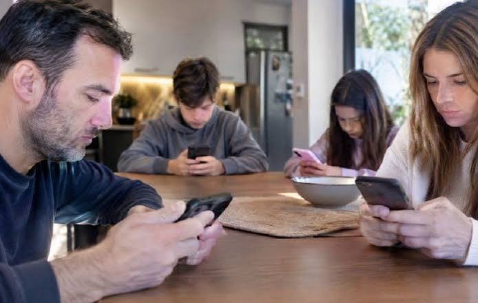 Familia en la mesa, cada uno usando su celular